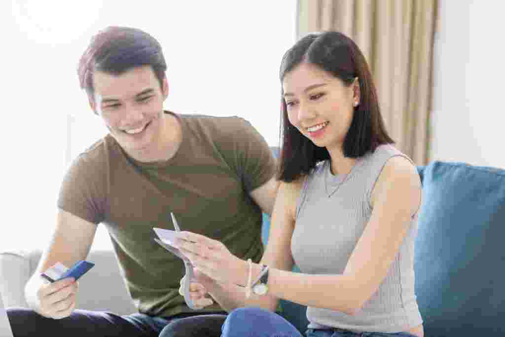 A smiling young couple cutting up credit cards with scissors after resolving debt and achieving financial freedom.