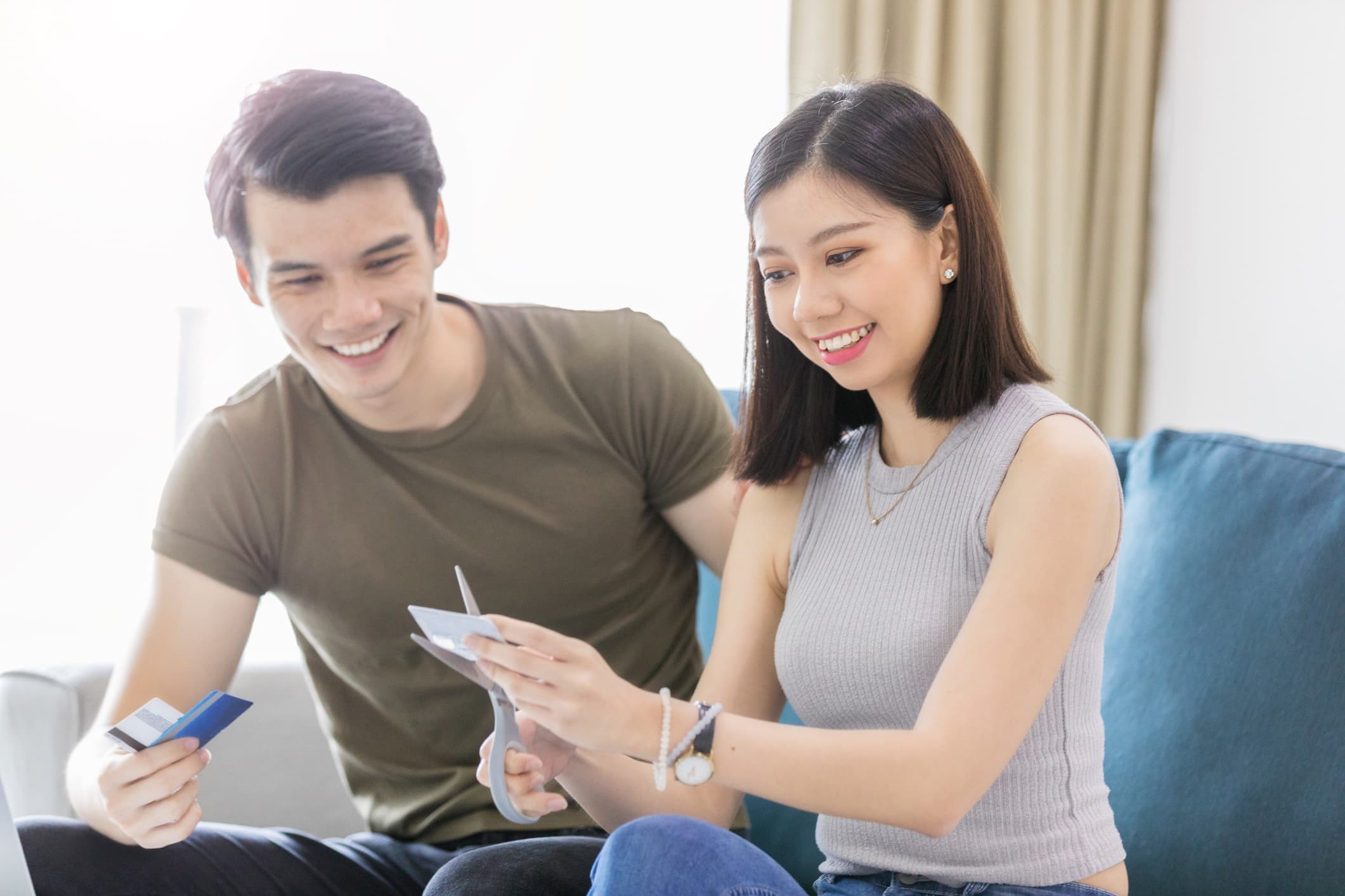 A smiling young couple cutting up credit cards with scissors after resolving debt and achieving financial freedom.
